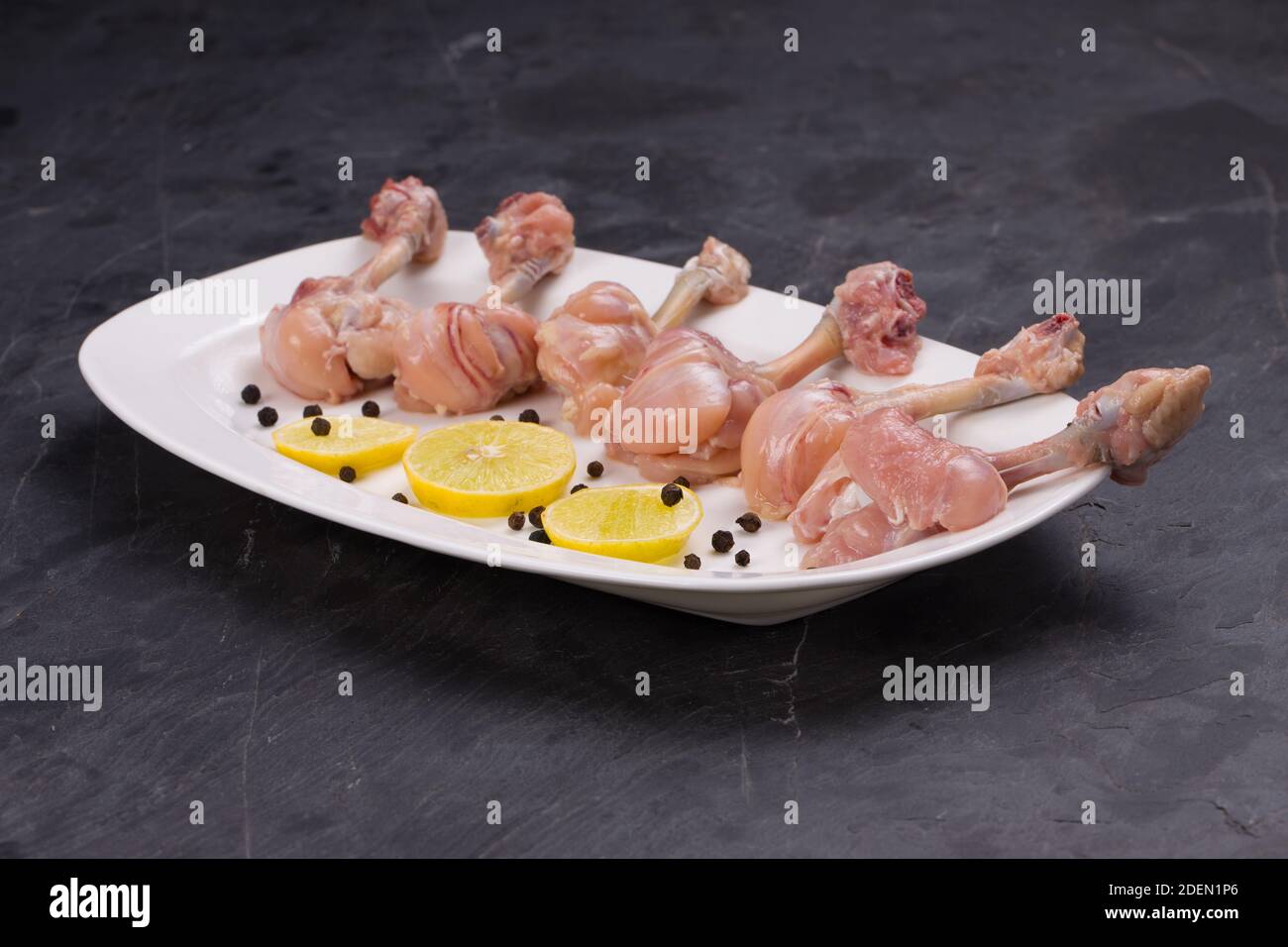 Rohes Huhn Lollipop, sechs Stücke Huhn Lollipop auf einem angeordnet Servierteller weiß und mit Zitronenscheiben und schwarz garniert Pfeffer auf grauer Textur Stockfoto