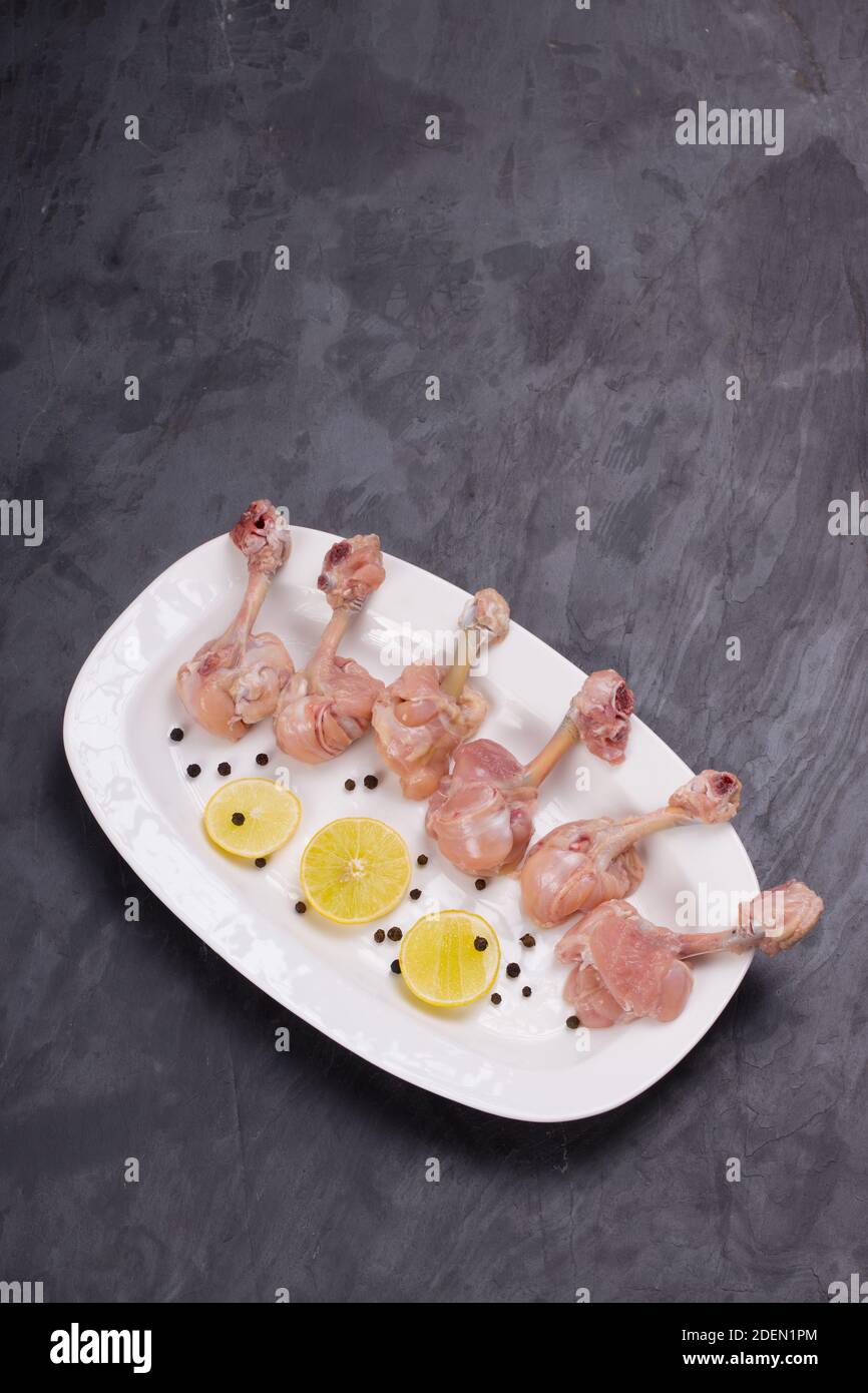 Rohes Huhn Lollipop, sechs Stücke Huhn Lollipop auf einem angeordnet Servierteller weiß und mit Zitronenscheiben und schwarz garniert Pfeffer auf grauer Textur Stockfoto
