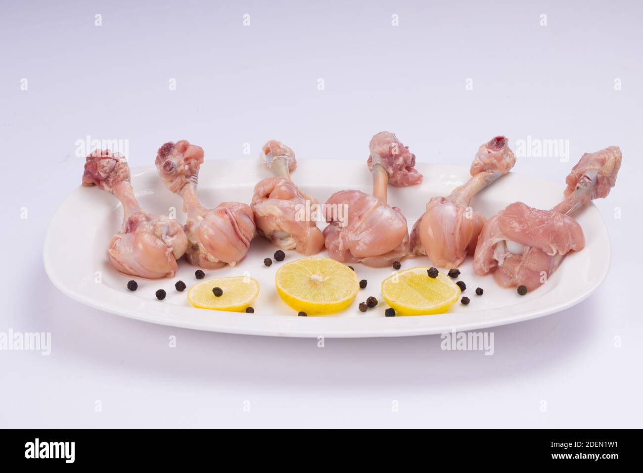Rohes Huhn Lollipop, sechs Stücke Huhn Lollipop auf einer Portion weißen Teller mit Zitronenscheiben und schwarzem Pfeffer auf weißem Hintergrund angeordnet Stockfoto