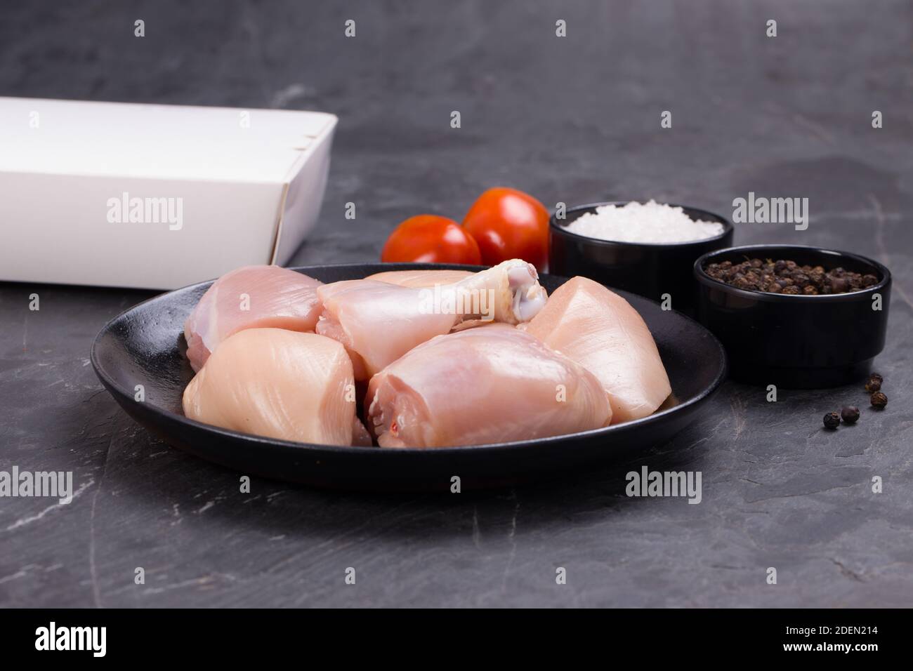 Rohes Huhn zartes Curry ohne Haut auf schwarz angeordnet geschnitten Teller mit Kochzutaten auf weißem Hintergrund mit Lieferkarton In der Nähe Stockfoto