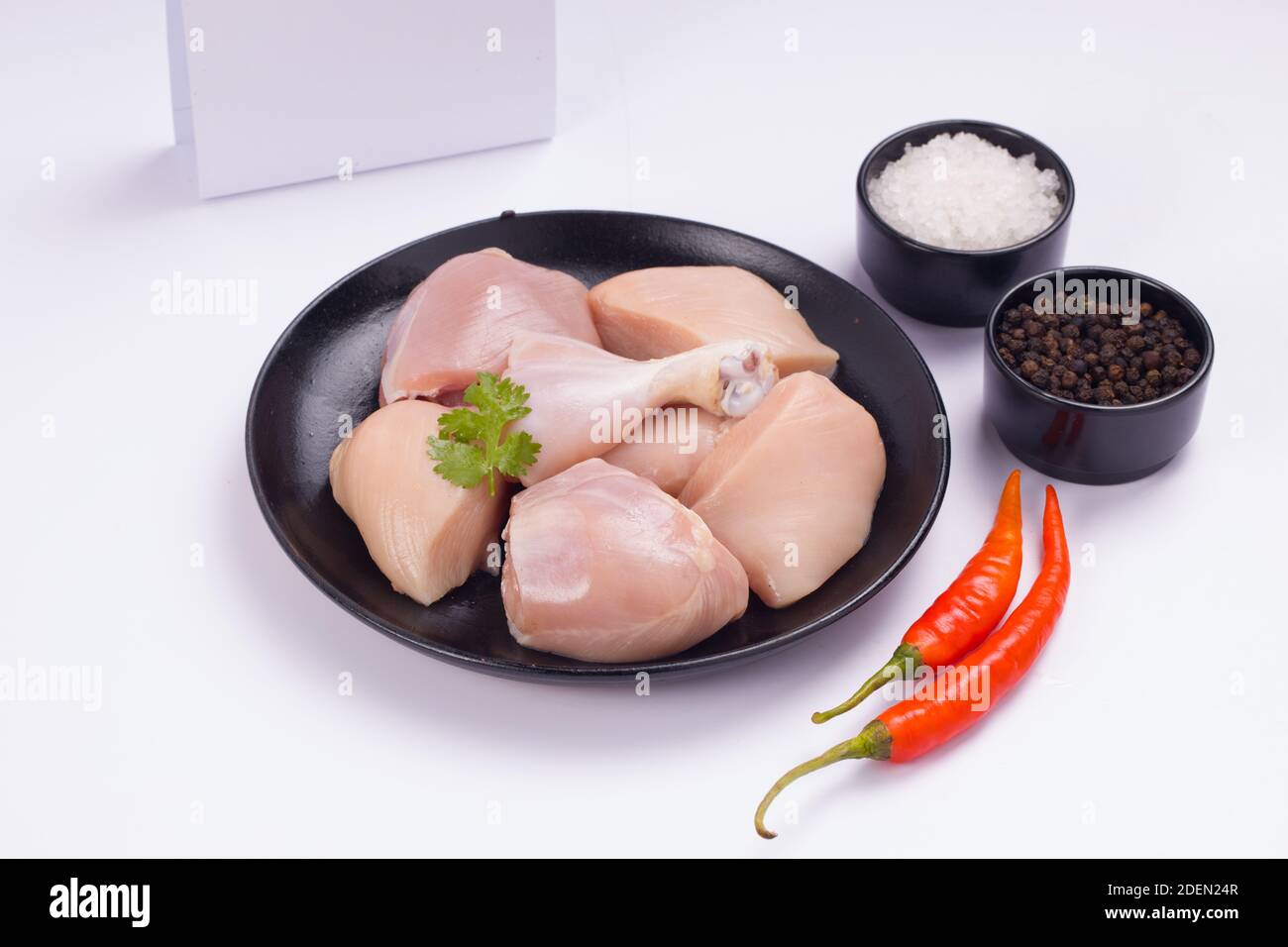 Rohes Huhn zartes Curry ohne Haut auf schwarzem Teller angeordnet geschnitten und mit rotem Chili, schwarzem Pfeffer und Salz auf weißem strukturierten Hintergrund garniert Stockfoto