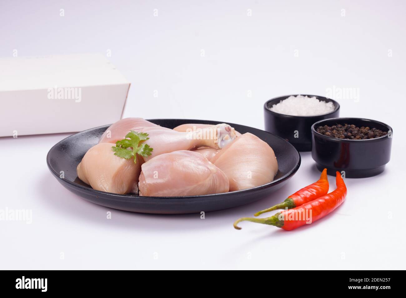 Rohes Huhn zartes Curry ohne Haut auf schwarzem Teller angeordnet geschnitten und mit rotem Chili, schwarzem Pfeffer und Salz auf weißem strukturierten Hintergrund garniert Stockfoto