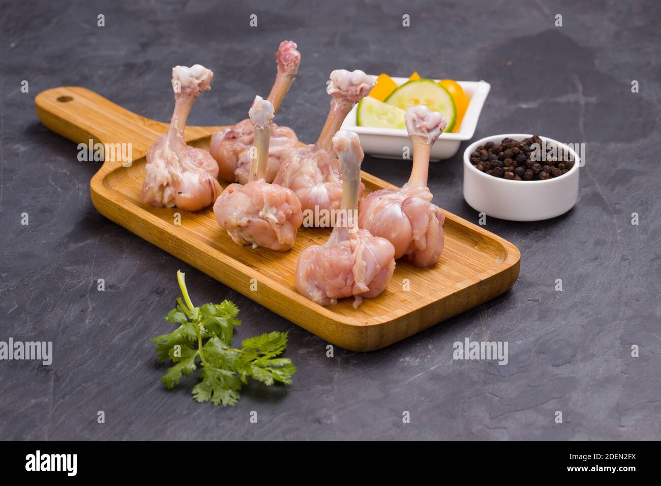 Rohes Huhn Lollipop, sechs Stücke Huhn Lollipop auf einem angeordnet Servierbrett mit schwarzem Pfeffer, Korianderblatt und Gurkenscheiben auf Hintergrund-wlan Stockfoto