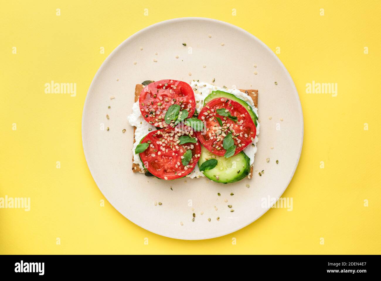Roggen-Knäckebrot oder Cracker mit veganem Frischkäse, Tomaten, Gurken und Hanfsamen isoliert auf gelbem Hintergrund. Draufsicht. Gesunde Vorspeise oder Snack Stockfoto