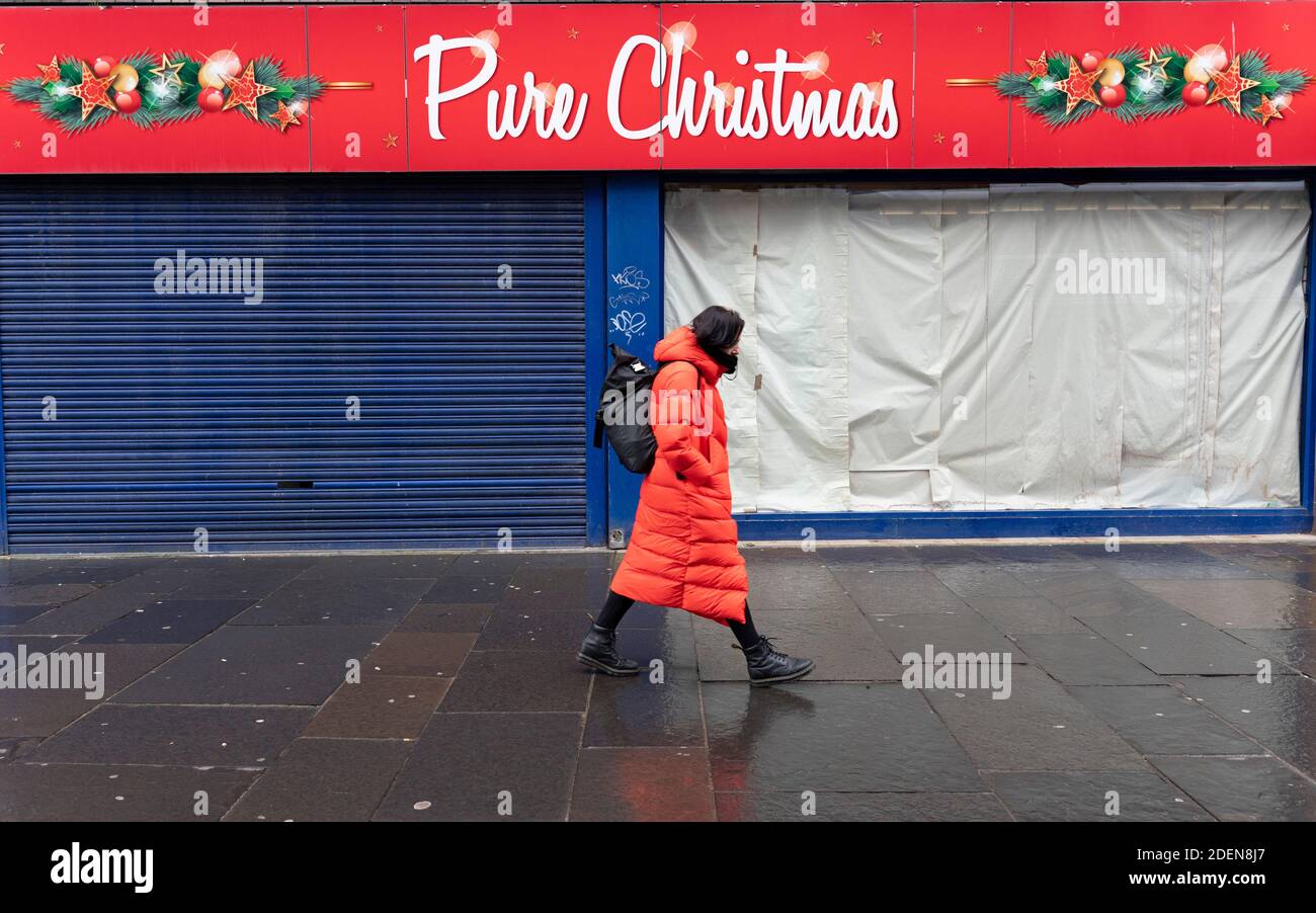 Glasgow, Schottland, UK.1. Dezember 2020. Coronavirus-Gesundheitswarnungen, Ladendisplay und Graffiti im Stadtzentrum von Glasgow. Im Bild: Frau in Rot geht an einem geschlossenen und verschlossenen Weihnachtsgeschäft vorbei. Iain Masterton/Alamy Live News Stockfoto