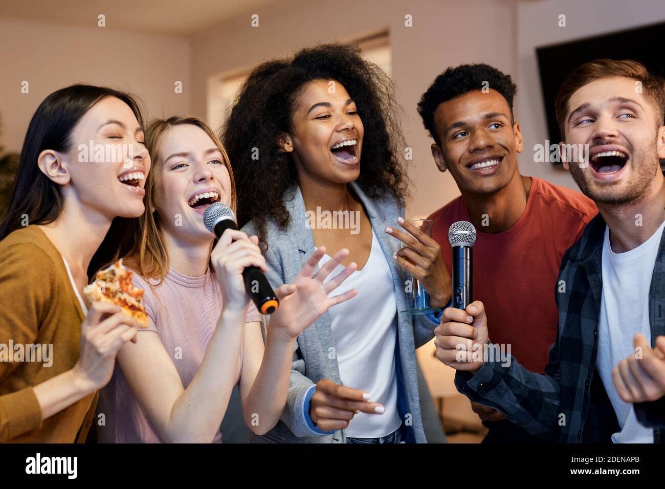 Singen Sie es. Enthusiastische Gruppe von Freunden, die mit Mikrofon  singen, während sie Karaoke zu Hause spielen und in der modernen Wohnung  stehen Stockfotografie - Alamy