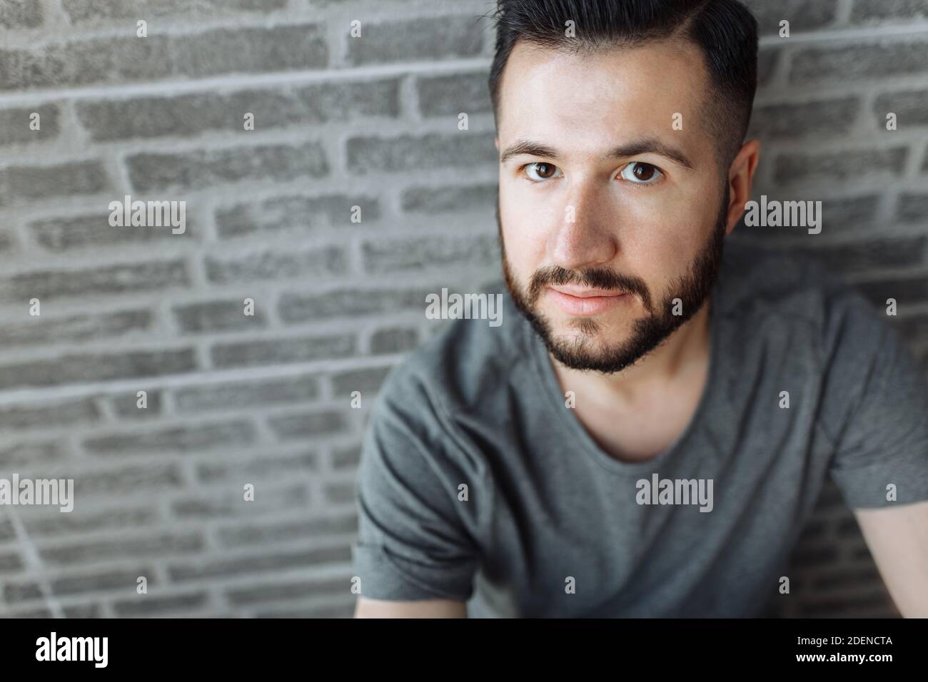 Porträt eines schönen stilvollen Kerl in einem grauen leeren T-Shirt gekleidet stehen auf einem Backstein grauen Wand Hintergrund. Stockfoto