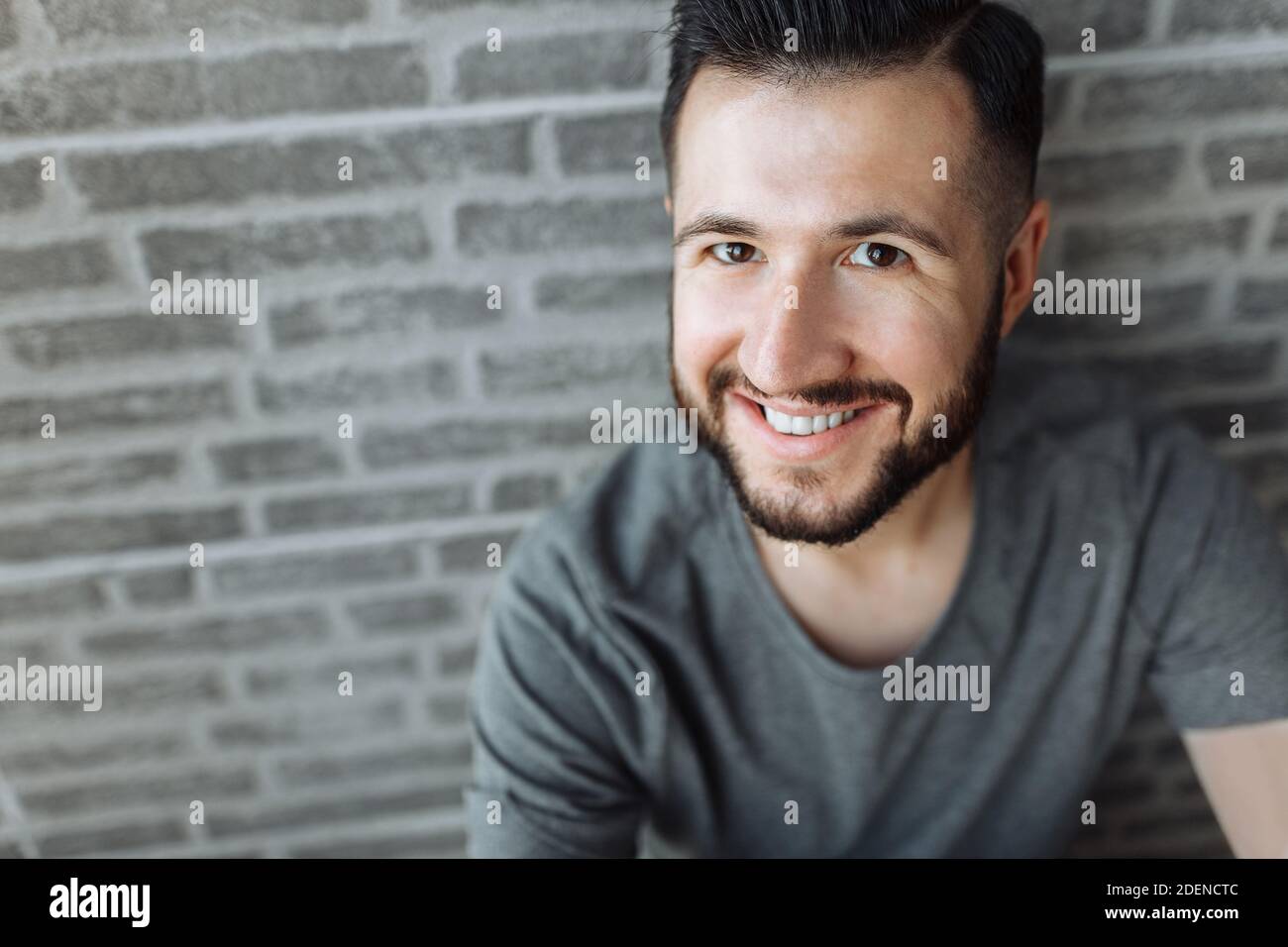 Porträt eines schönen stilvollen Kerl in einem grauen leeren T-Shirt gekleidet stehen auf einem Backstein grauen Wand Hintergrund. Stockfoto