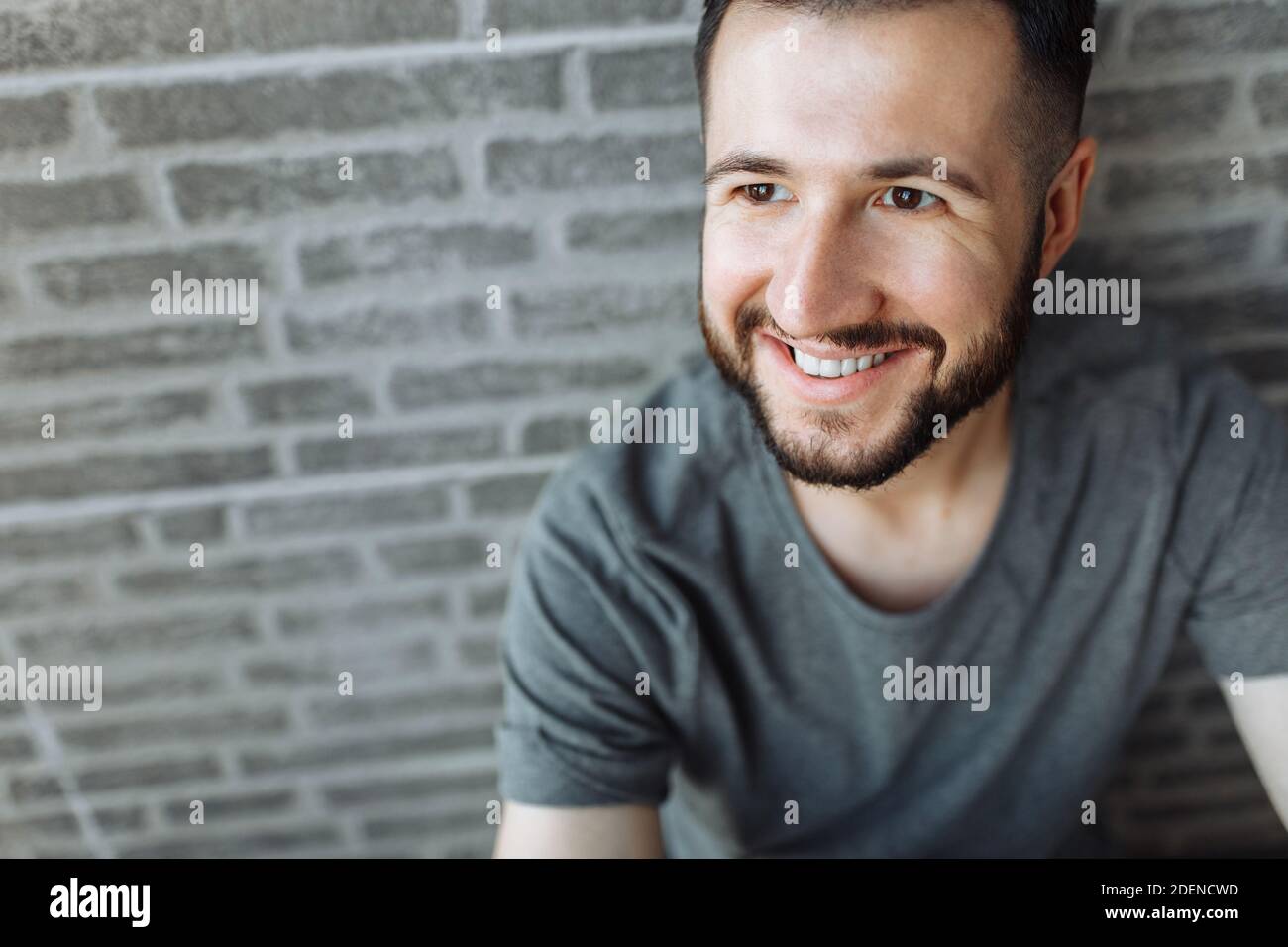 Porträt eines schönen stilvollen Kerl in einem grauen leeren T-Shirt gekleidet stehen auf einem Backstein grauen Wand Hintergrund. Stockfoto