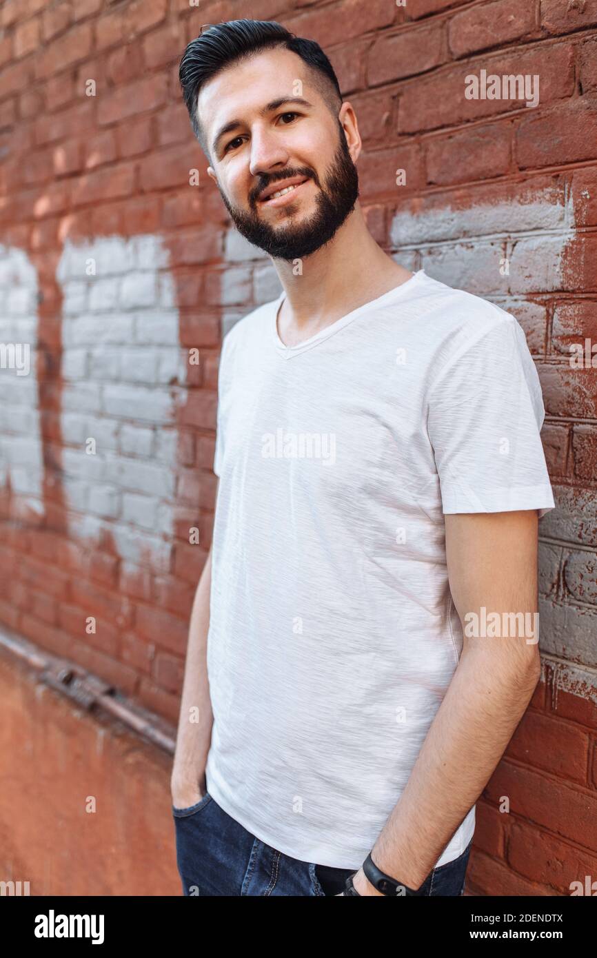 Porträt eines stylischen und positiven Guy, in einem weißen leeren T-Shirt, an der orangen Backsteinwand, Stockfoto