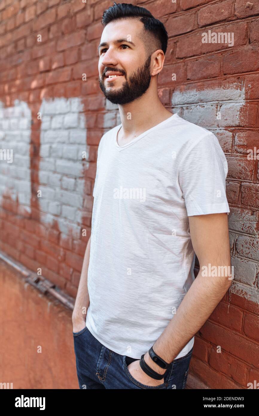 Porträt eines stylischen und positiven Guy, in einem weißen leeren T-Shirt, an der orangen Backsteinwand, Stockfoto