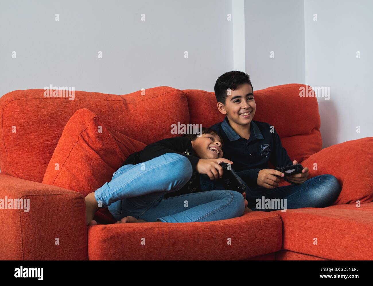 Ein sehr glückliches und lächelndes Mädchen und Jungen, die zu Hause auf dem Sofa sitzen und Videospiele spielen. Stockfoto