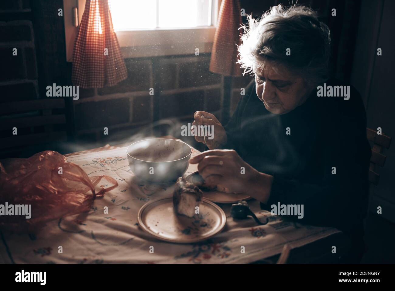 Ältere Frau, die allein am Tisch sitzt und eine Mahlzeit isst Stockfoto