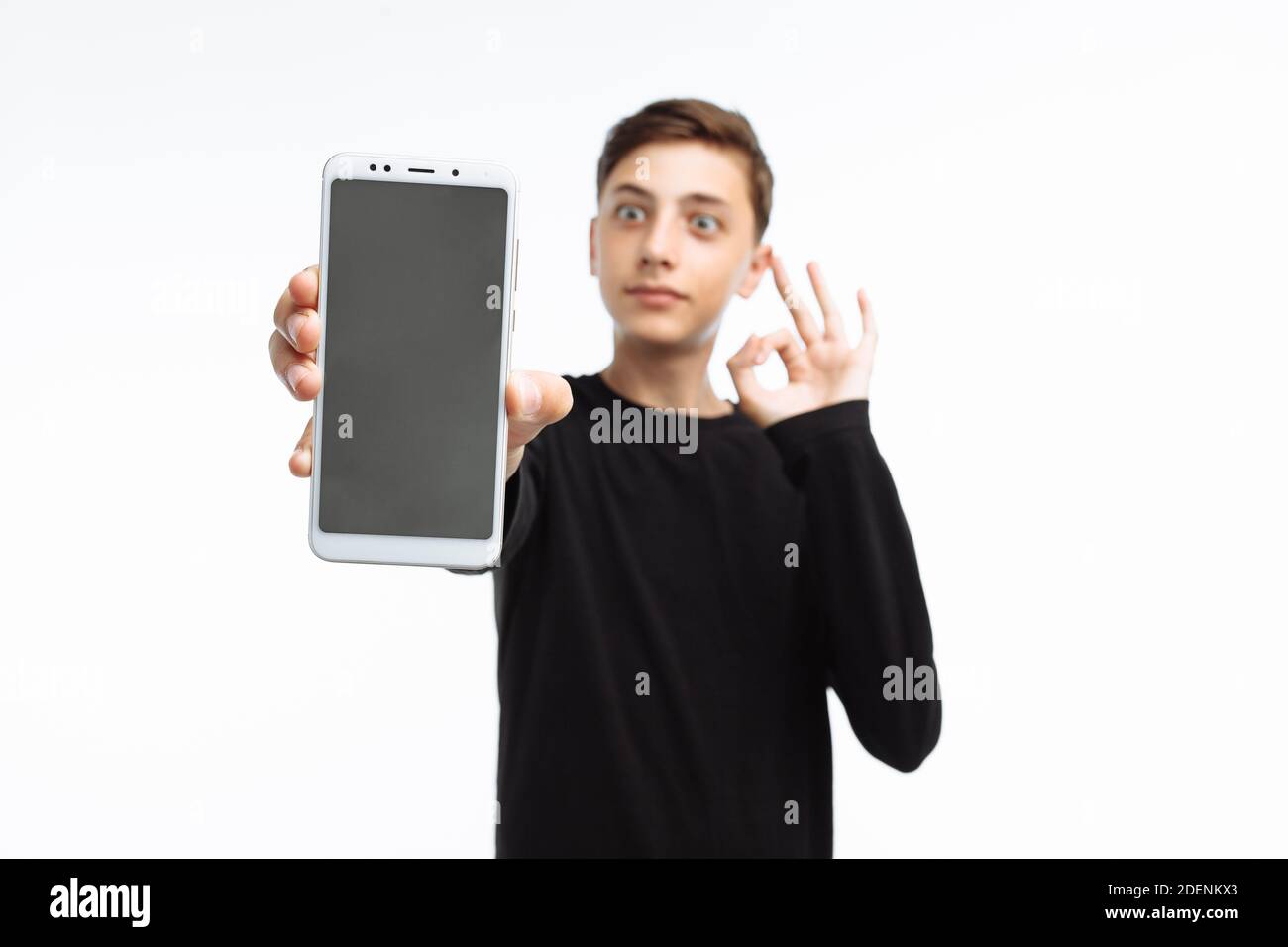 Porträt eines Teenagers, eines Mannes, der ein Telefon mit einem weißen Bildschirm hält, und zeigt einen Finger auf dem Bildschirm, in einem schwarzen T-Shirt, auf einem weißen Hintergrund, Stockfoto