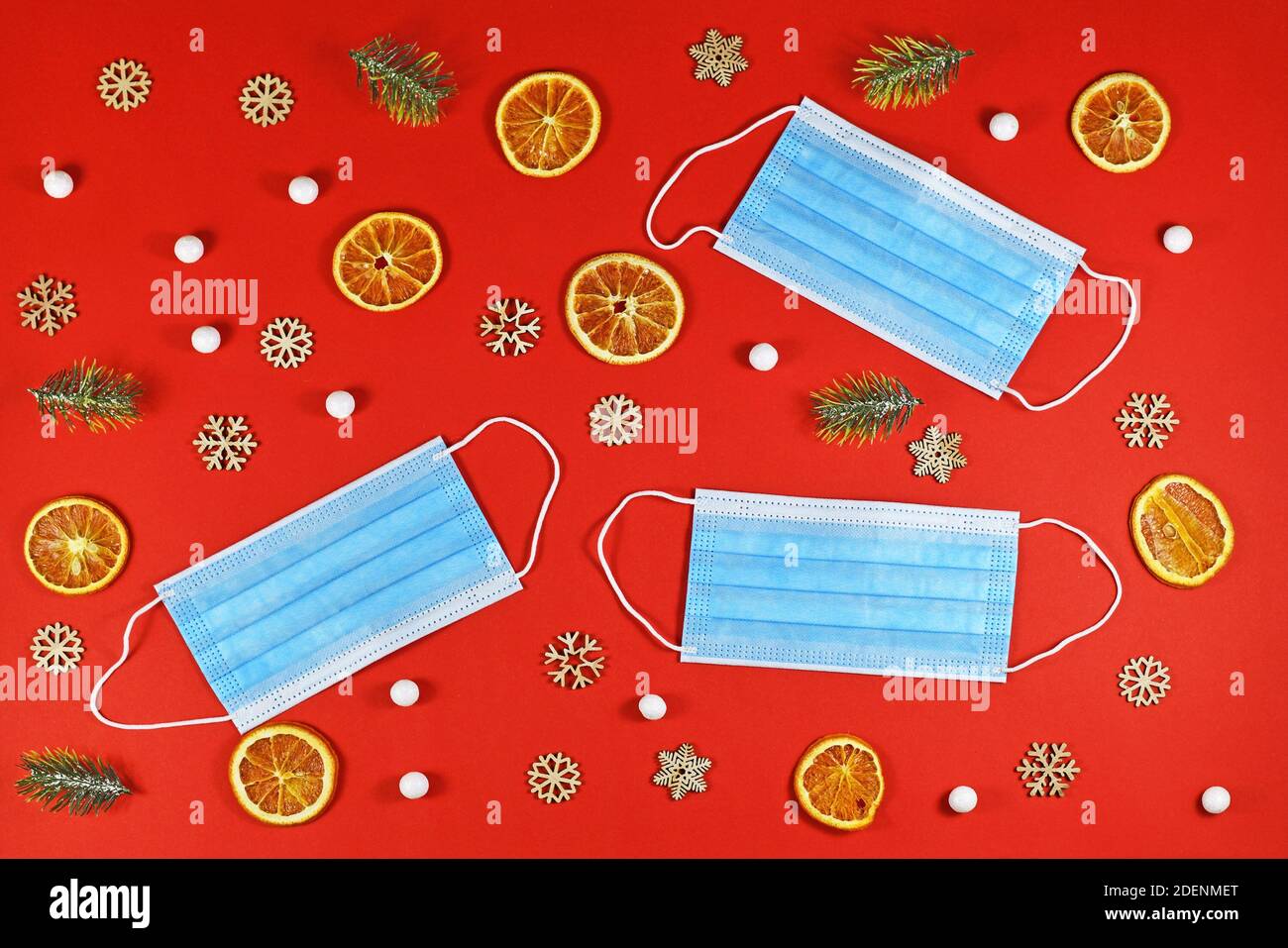 Weihnachten während der Corona Virus Times Konzept mit medizinischer Gesichtsmaske Umgeben von festlichen Weihnachtsornamenten auf rotem Hintergrund Stockfoto