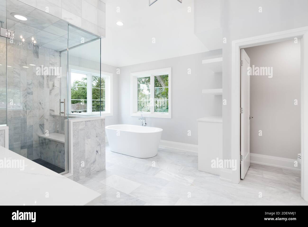 Ein großes luxuriöses Badezimmer mit einer freistehenden Badewanne, weißem Waschtisch und einer Duschkabine aus Glas mit Marmorfliesen und Sitzbank. Stockfoto