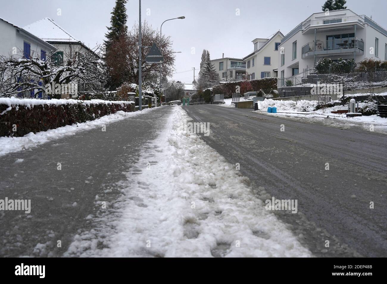 Straße und Gehweg in der Straße von Urdorf in der Schweiz im Winter. Sie sind mit gestampftem schmutzigem Schnee bedeckt und mit Straßensalz behandelt. Stockfoto