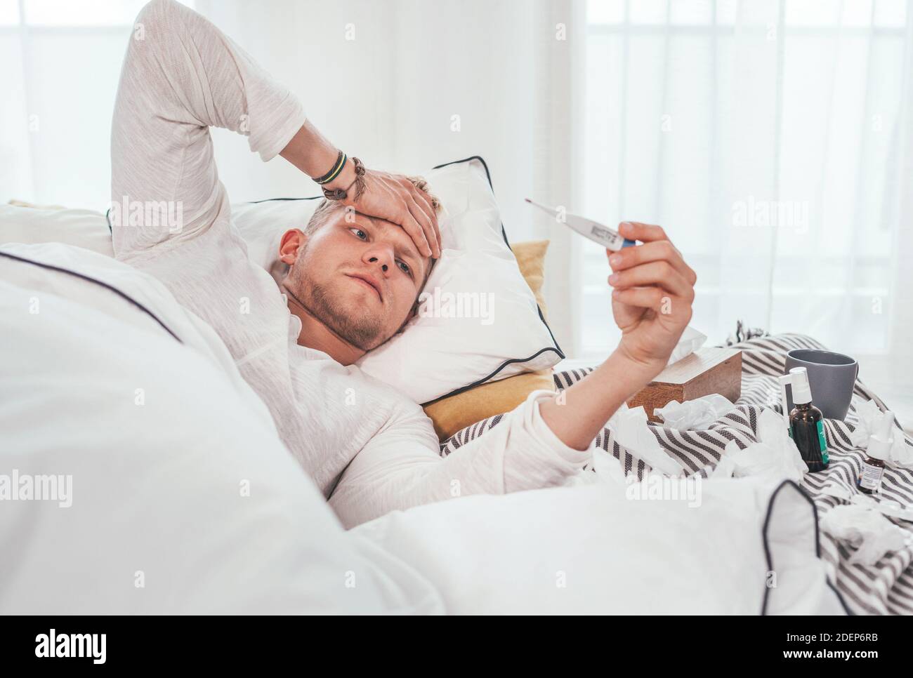 Müde und ungesund Blick auf ein medizinisches Thermometer wie in einem gemütlichen Bett neben einer Menge von gebrauchten Papiertaschentücher und Medikamente auf der Decke liegen. Meere Stockfoto