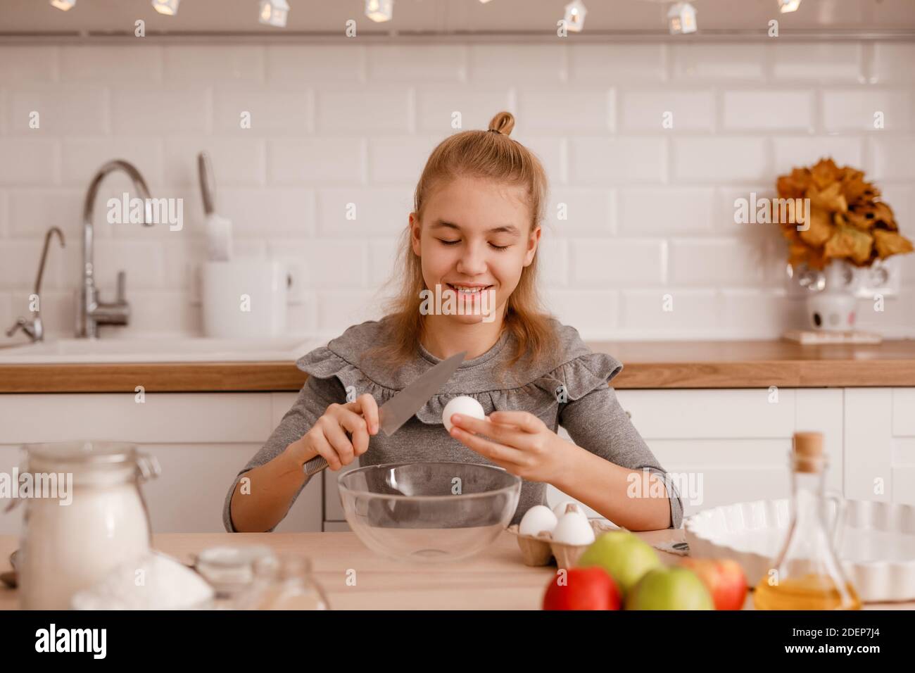 Blonde Teenager-Mädchen in einem grauen Kleid wird traditionelle Apfelkuchen in der neuen Küche kochen. Stockfoto