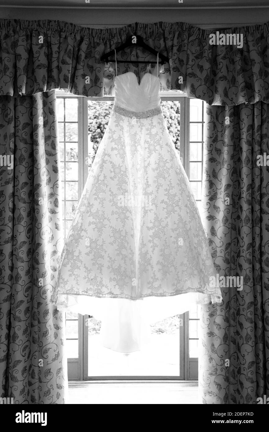 Hintergrundbeleuchtetes weißes Hochzeitskleid mit Tapeten, das im Fenster oder an der Tür hängt Stockfoto