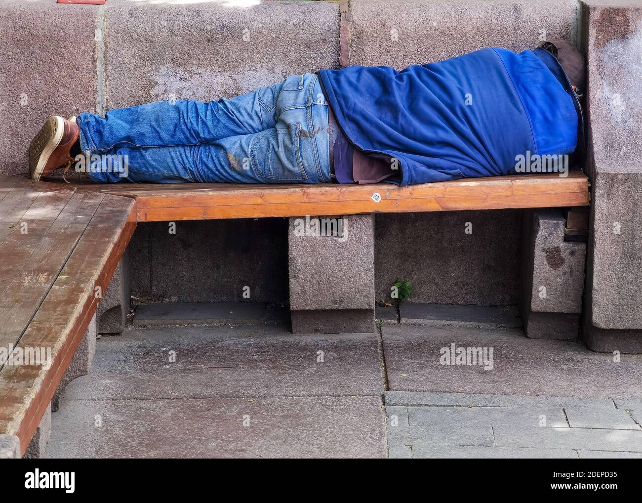 Obdachloser, der tagsüber auf einer hölzernen Parkbank schlecht schläft. Ein Symbol für die wachsenden Probleme der Obdachlosigkeit und Armut vor allem in der citi Stockfoto