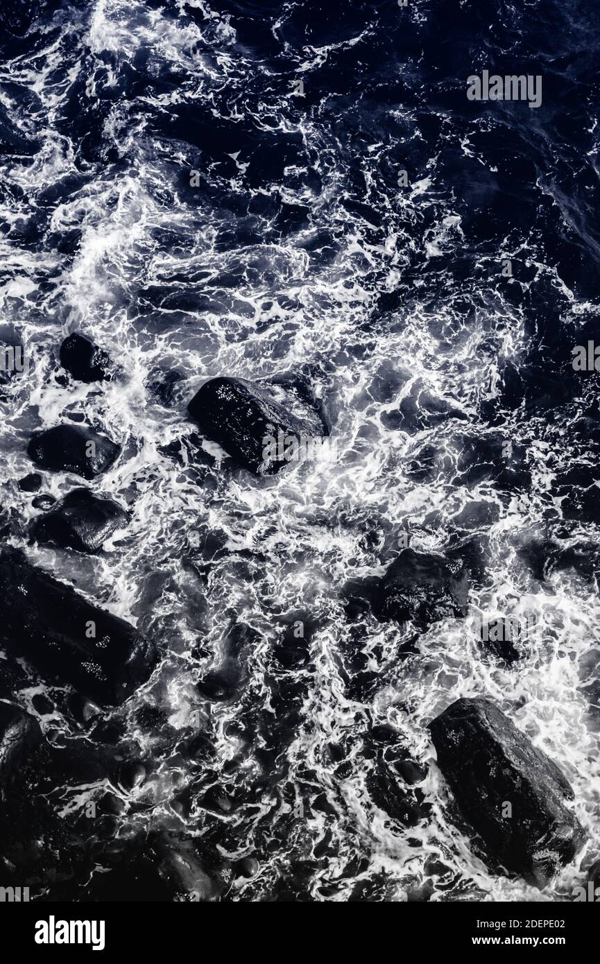 Wasser und Felsen (Duoton) . Kleine Wellen stürzen auf eine felsige Küste und erzeugen Wirbelwinde aus weißem Schaum, von oben gesehen Stockfoto