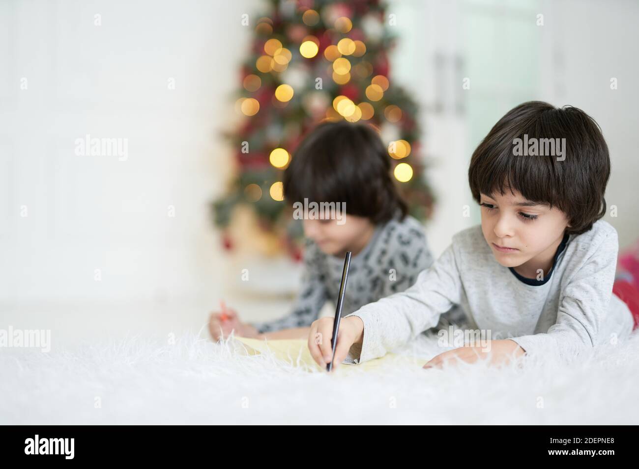 Zwei kleine lateinische Jungen, Zwillinge zeichnen Bilder mit bunten Bleistiften, während sie auf dem Boden zu Hause für Weihnachten geschmückt liegen. Kindheit, Familie, Winterurlaub Konzept Stockfoto