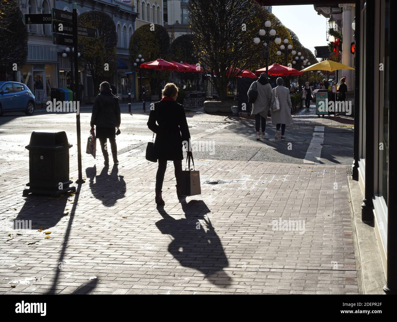 Die Käufer werfen Schatten, während sie von der Morgensonne entlang der Government Street in Victoria, British Columbia, Kanada, umrahmt werden Stockfoto