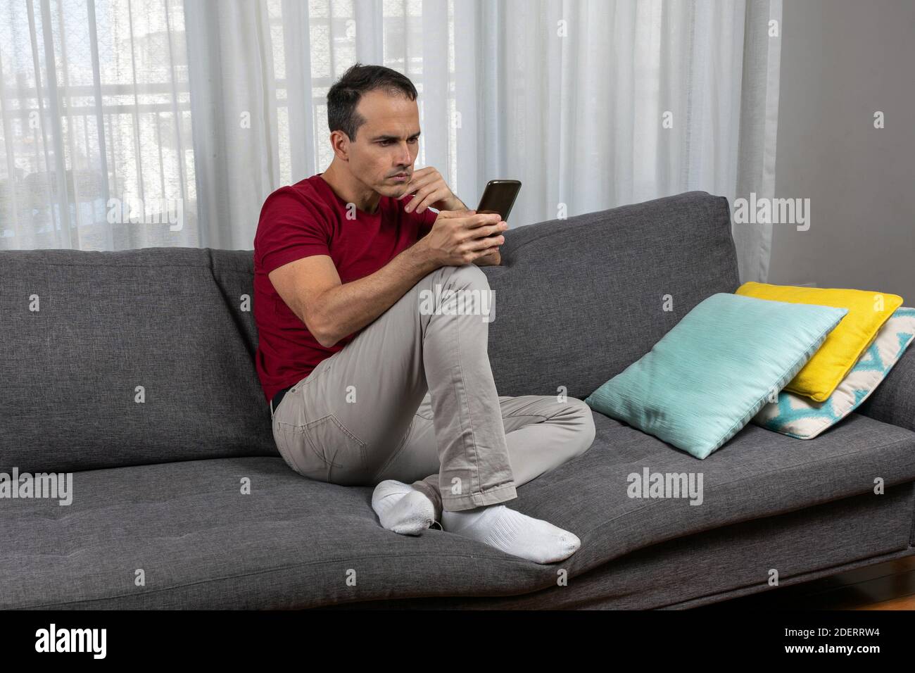 Reifer Mann (44 Jahre) sitzt mit seinen Socken auf der Couch und fiddelt mit seinem Smartphone. Stockfoto