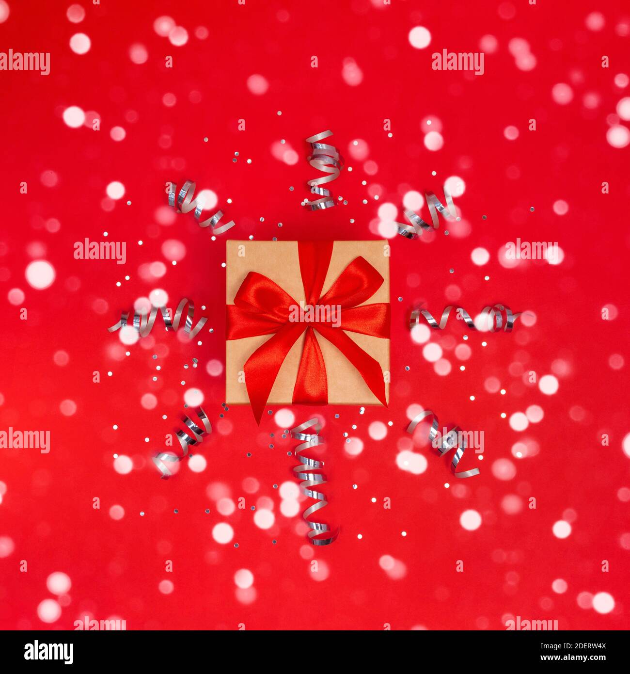 Geschenkbox mit Band mit Konfetti, Schnee und funkelt auf rotem Hintergrund. Weihnachten, Neujahr, Party, Geburtstagsgeschenk. Flay Lay with copy space Stockfoto