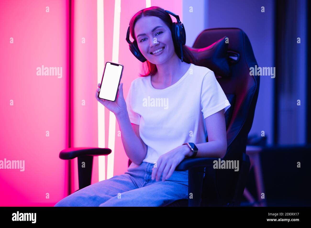 Glückliche Gamer Mädchen tragen Headset zeigt Smartphone-Display und zeigt auf leeren Bildschirm mit ihrem Finger. Stockfoto