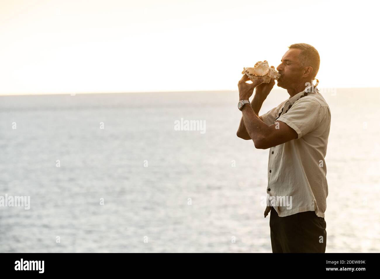 Männlicher Beamter bläst Muschelschale in hawaii am Ozean Stockfoto
