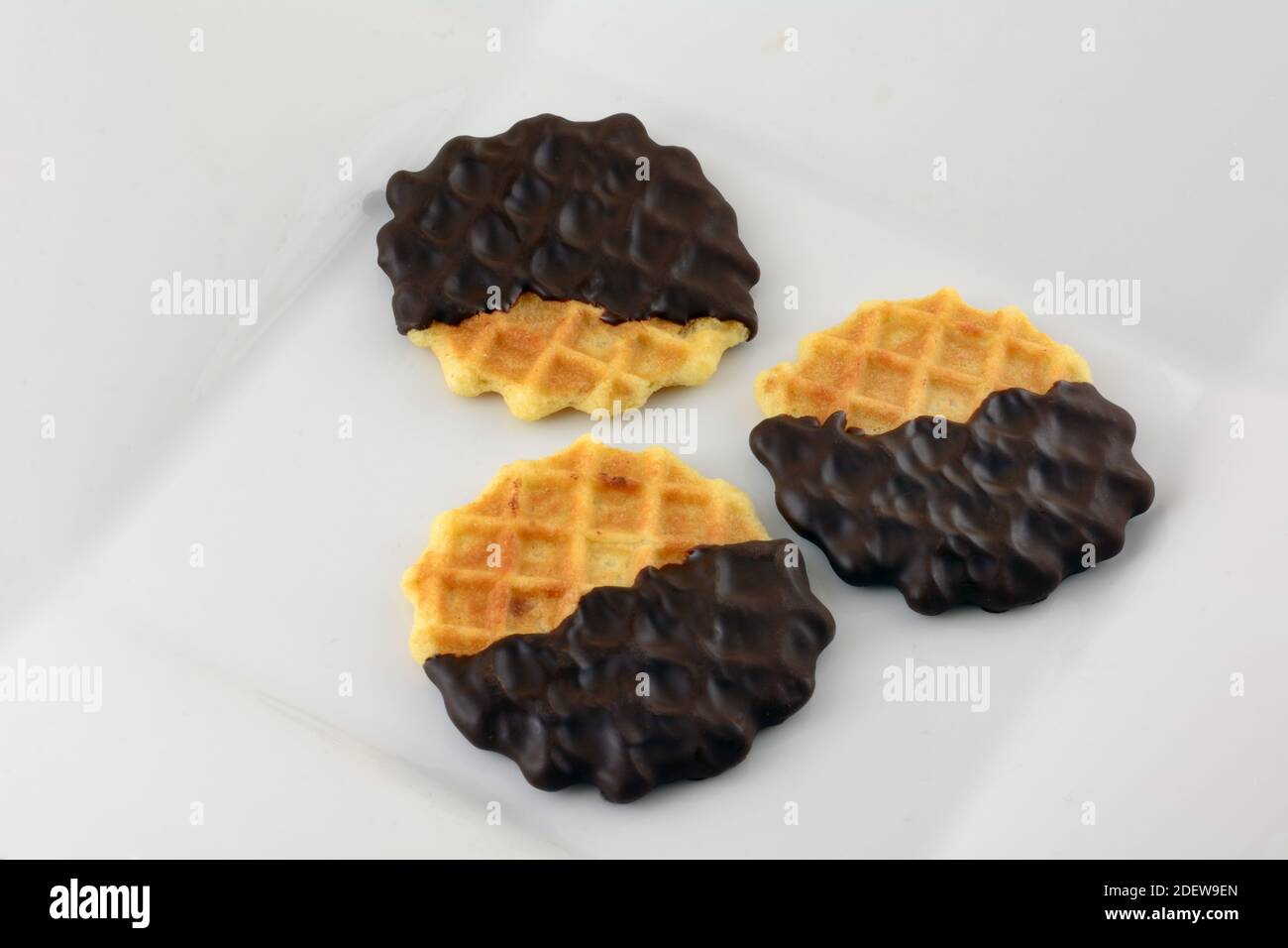 Drei dunkle, in Schokolade getauchte Waffelplätzchen auf weißem Snackteller Stockfoto