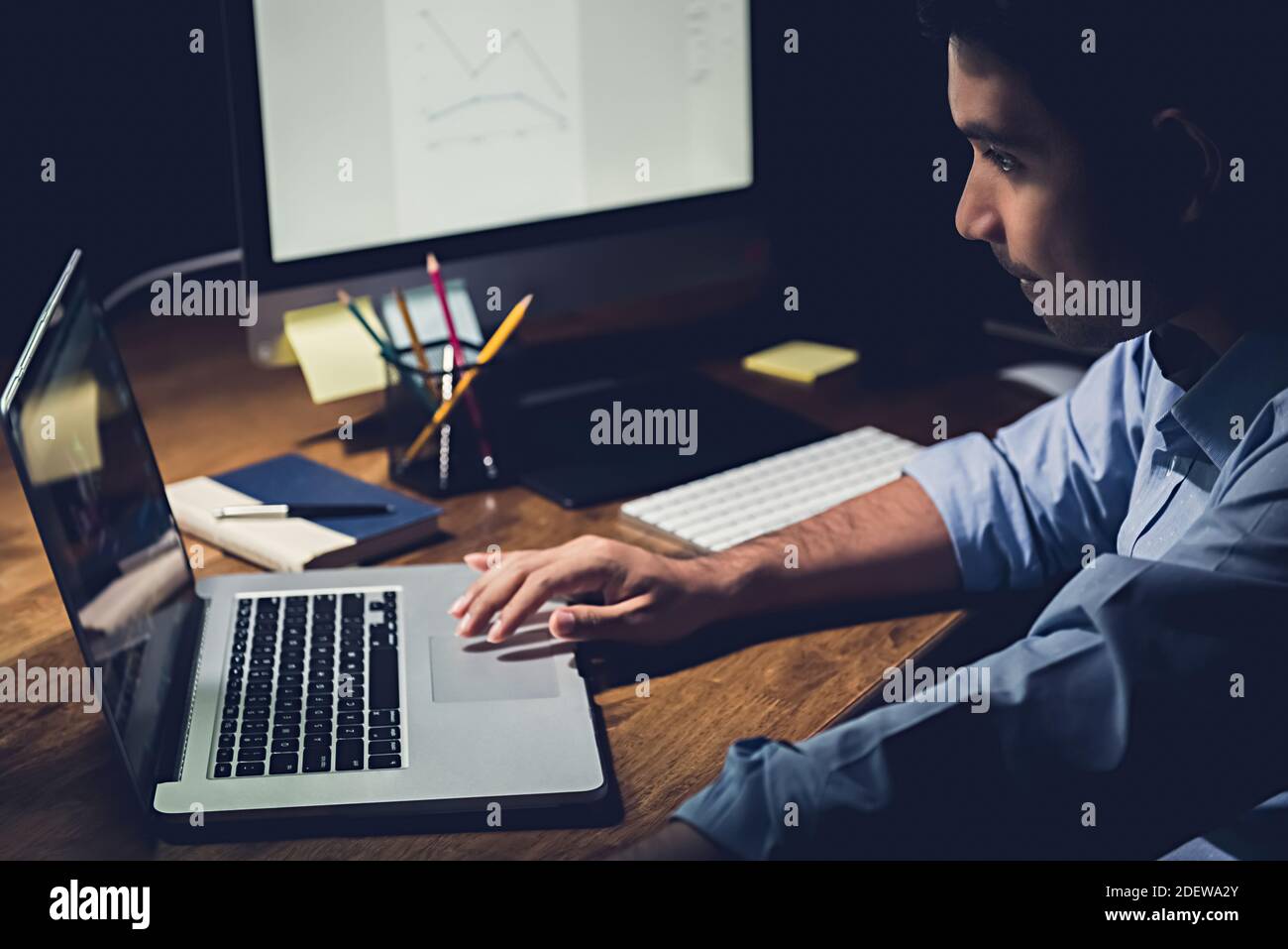 Junger Geschäftsmann, der spät in der Nacht im Büro Überstunden hat Der Schwerpunkt liegt auf der Arbeit mit einem Laptop an seinem Schreibtisch Stockfoto