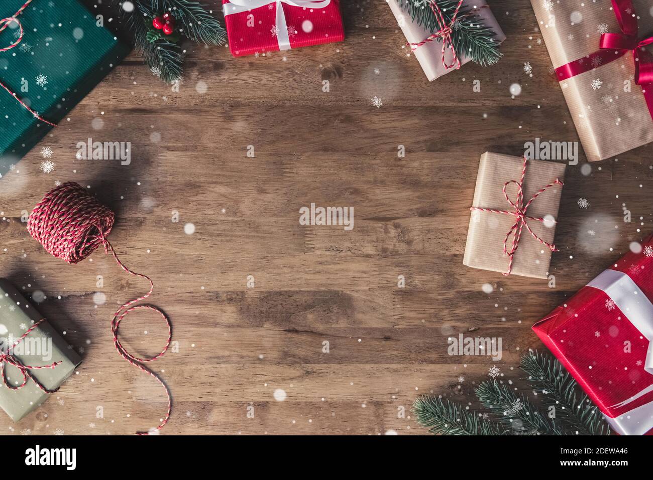 Draufsicht auf bunt dekorierte Geschenkboxen auf einem Holztisch mit fallendem Schnee-Effekt, Bordüre Design Weihnachten Hintergrund mit Kopierraum in der Mitte Stockfoto