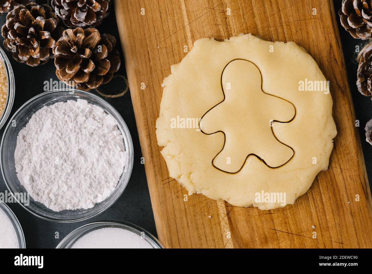 Weihnachts-Ingwer-Brot-Mann-Plätzchen-Cutter in rohem Plätzchenteig mit Pinienzapfen, Feiertagsrippen und Zutaten auf dunkler Schieferstruktur Stockfoto