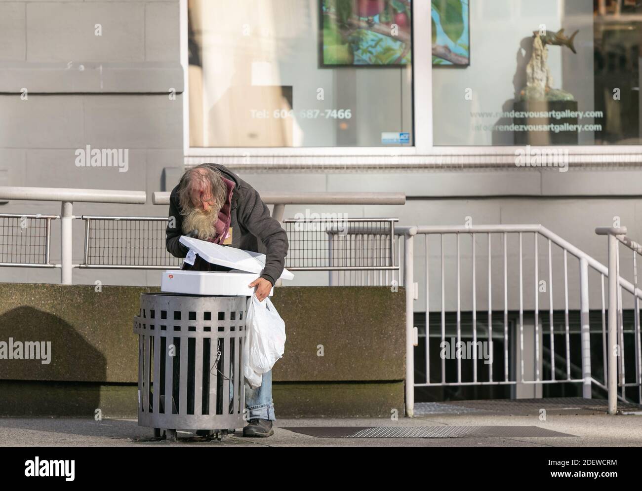 Ein Obdachloser, der in einem Müllcontainer nach Essen sucht. Vancouver, BC, Kanada - November 1,2020. Selektiver Fokus, Straßenbild, Stadtarmut. Stockfoto
