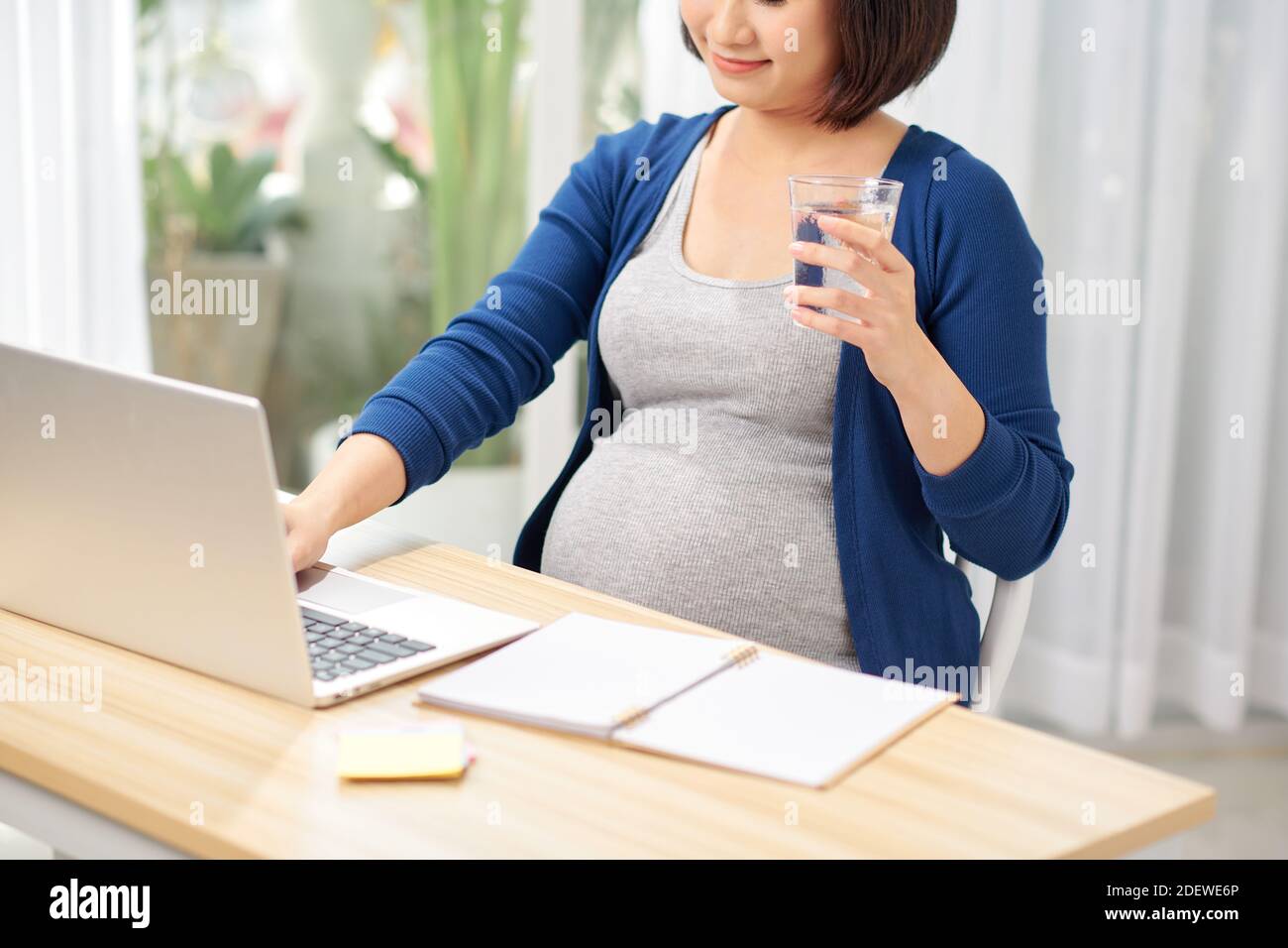 Schwangere Frau im Home Office in der Nähe von Tisch mit Computer und Trinkwasser Stockfoto