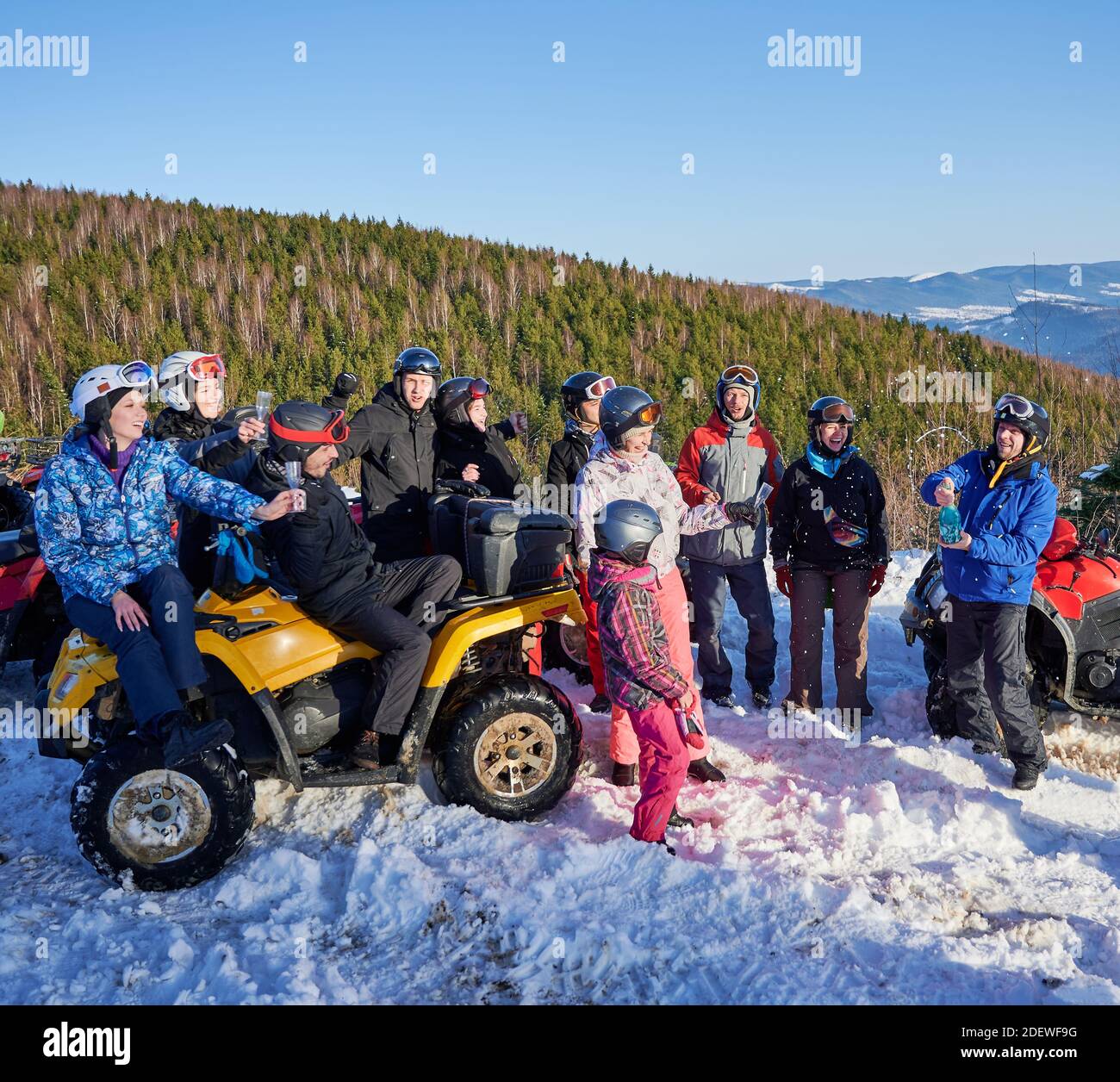 Gruppe von fröhlichen Menschen sitzen auf vier Rädern ATV, genießen schönen Wintertag in verschneiten Bergen, Entkorken Flasche blauen Champagner. Feiern Sie im Freien. Konzept des aktiven Lebensstils Stockfoto