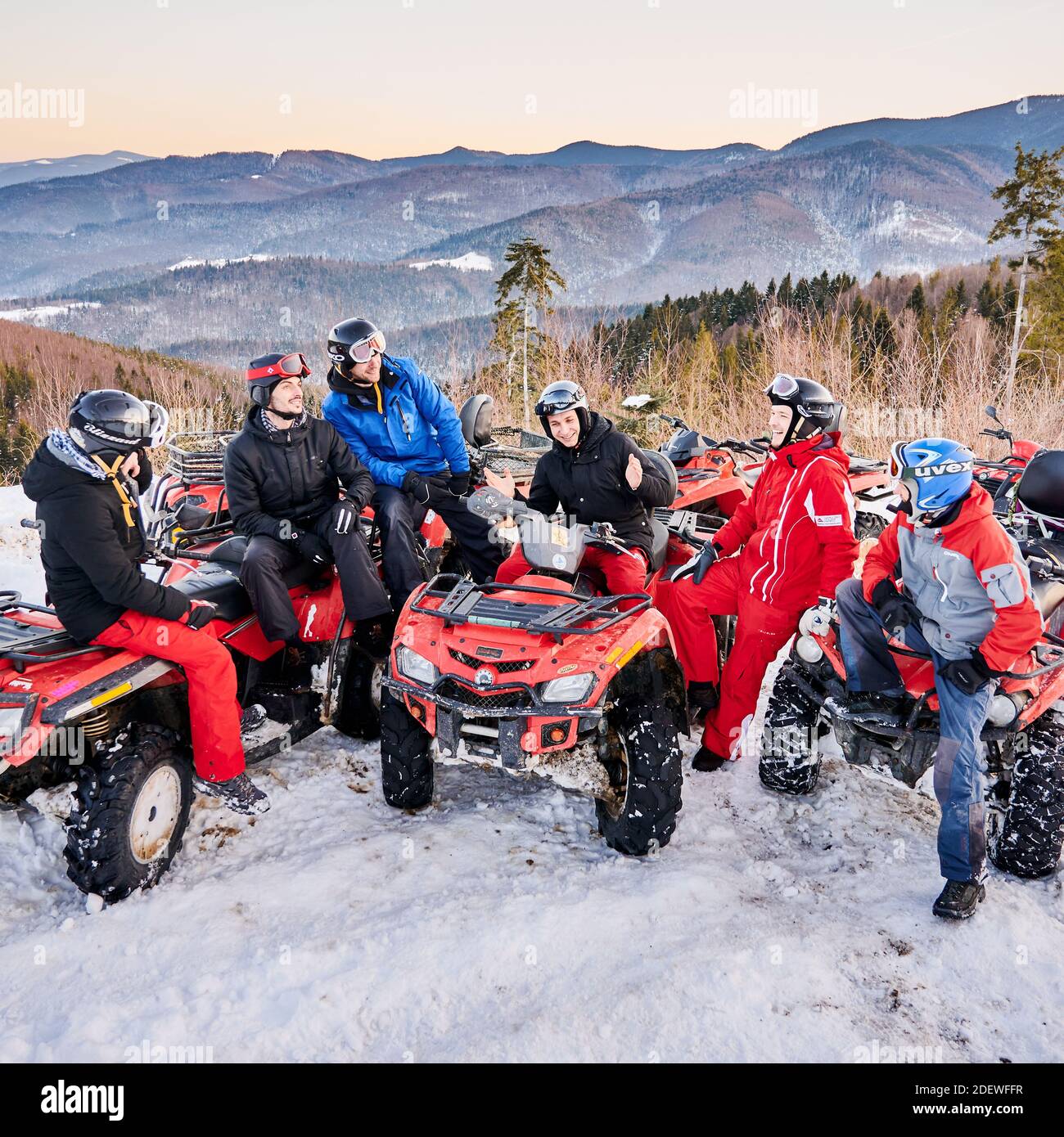Yaremche, Ukraine - 02. Februar 2020: Gruppe von Männern, die auf ATV-Fahrrädern sitzen, kleine Gespräche führen und am kalten Wintertag in verschneiten Bergen lachen, Bergrücken im Hintergrund. Konzept der Freundschaft Stockfoto