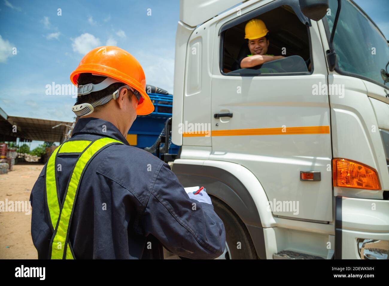 Asiatischer Vorarbeiter mit Sicherheitshüten und Sicherheitsweste trägt ein Auto-Inspektionsdokument auf dem Parkplatz mit LKW-Fahrer, Konzept der Planung Arbeitstag. R Stockfoto