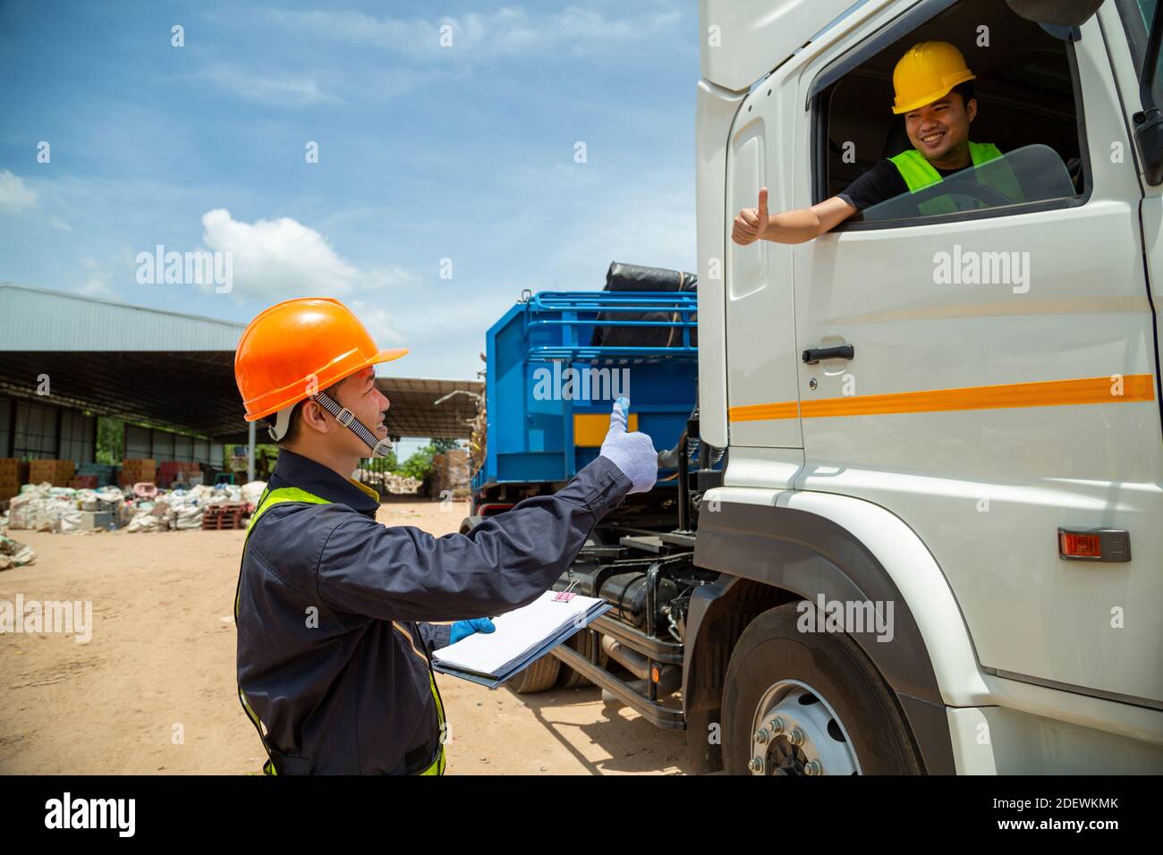 Asiatischer Vorarbeiter mit Sicherheitshüten und Sicherheitsweste trägt ein Auto-Inspektionsdokument auf dem Parkplatz mit LKW-Fahrer, Konzept der Planung Arbeitstag. R Stockfoto