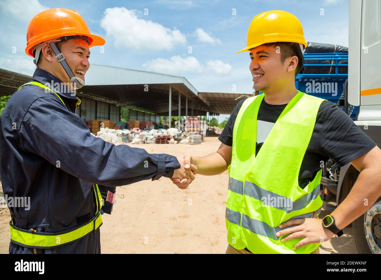 Asiatischer Vorarbeiter mit Schutzhüten und Sicherheitsweste trägt Ein Auto-Inspektionsdokument im Parkplatz Handschlag mit LKW Treiber,Planungskonzept w Stockfoto