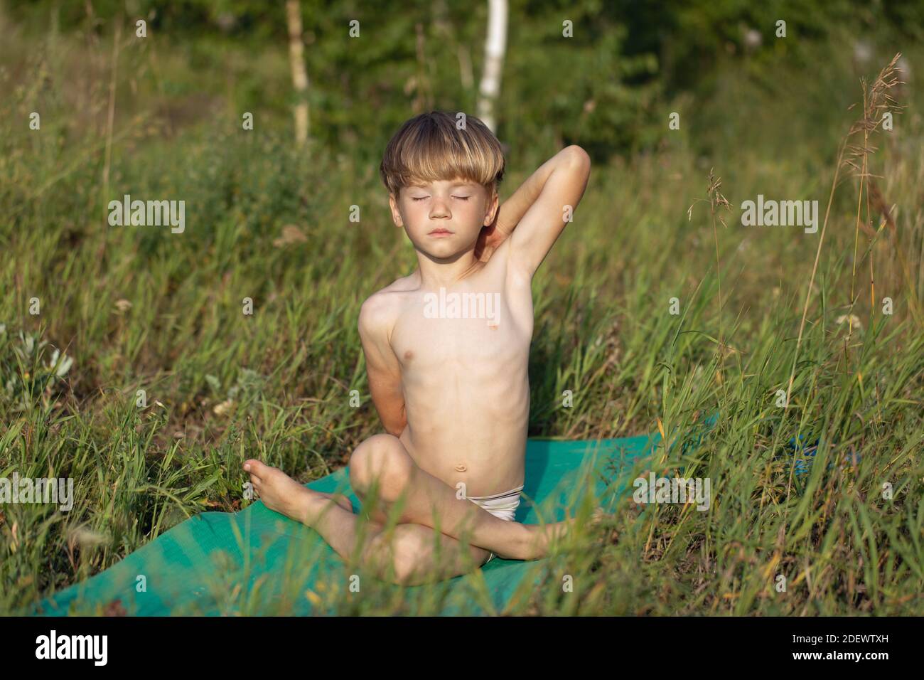 Portrait des Jungen Kind Yoga praktizieren, sitzen in Gomukhasana Übung, Kuh Gesicht Pose draußen im Park trainieren Stockfoto