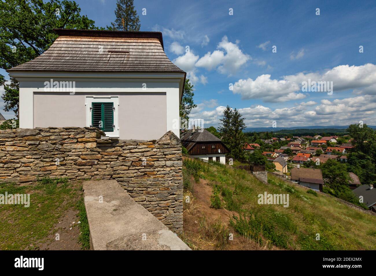 Opocno, Tschechische Republik - Juni 16 2020: Blick auf die Stadt und Häuser von einem Friedhof mit einer Kapelle mit Schindeldach hinter Steinmauer. Sonnig. Stockfoto