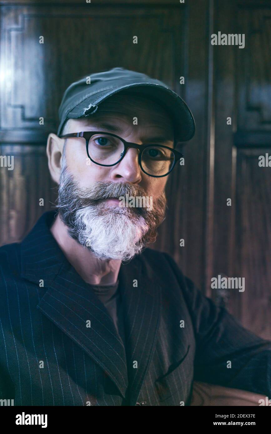 Nahaufnahme Porträt einer männlichen Figur mittleren Alters tragen Brille und eine Kappe mit einem langen Bart Blick auf die Kamera. Stockfoto