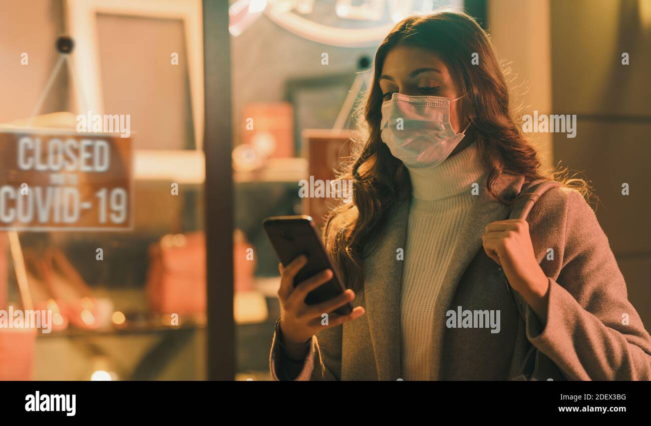 Shop geschlossen wegen Coronavirus Ausbruch und Frau mit ihrem Smartphone verbinden, trägt sie eine chirurgische Maske Stockfoto
