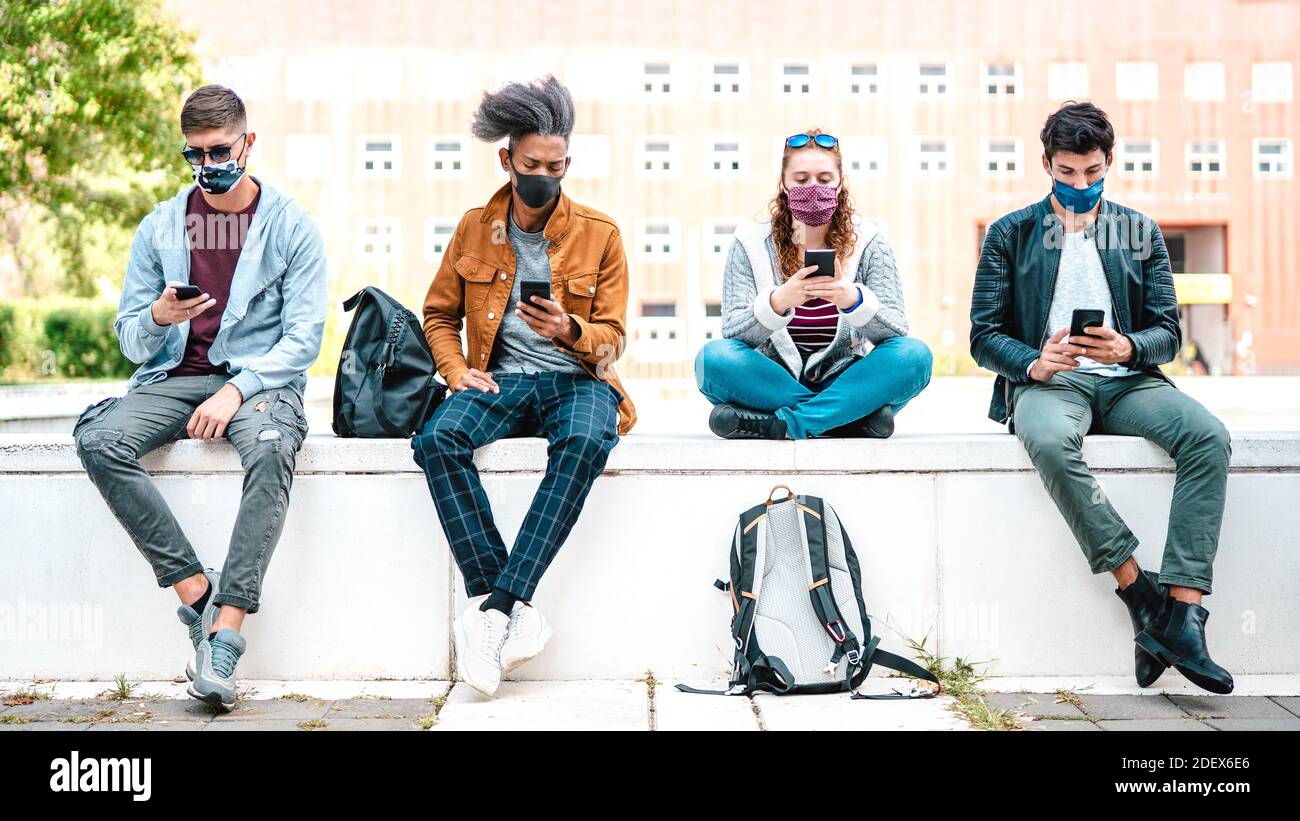 Millennial Freunde mit Smartphones mit Gesichtsmaske auf Covid Zweite Welle - besorgt Jungs und Mädchen, die Nachrichten auf Mobiles Smartphone Stockfoto