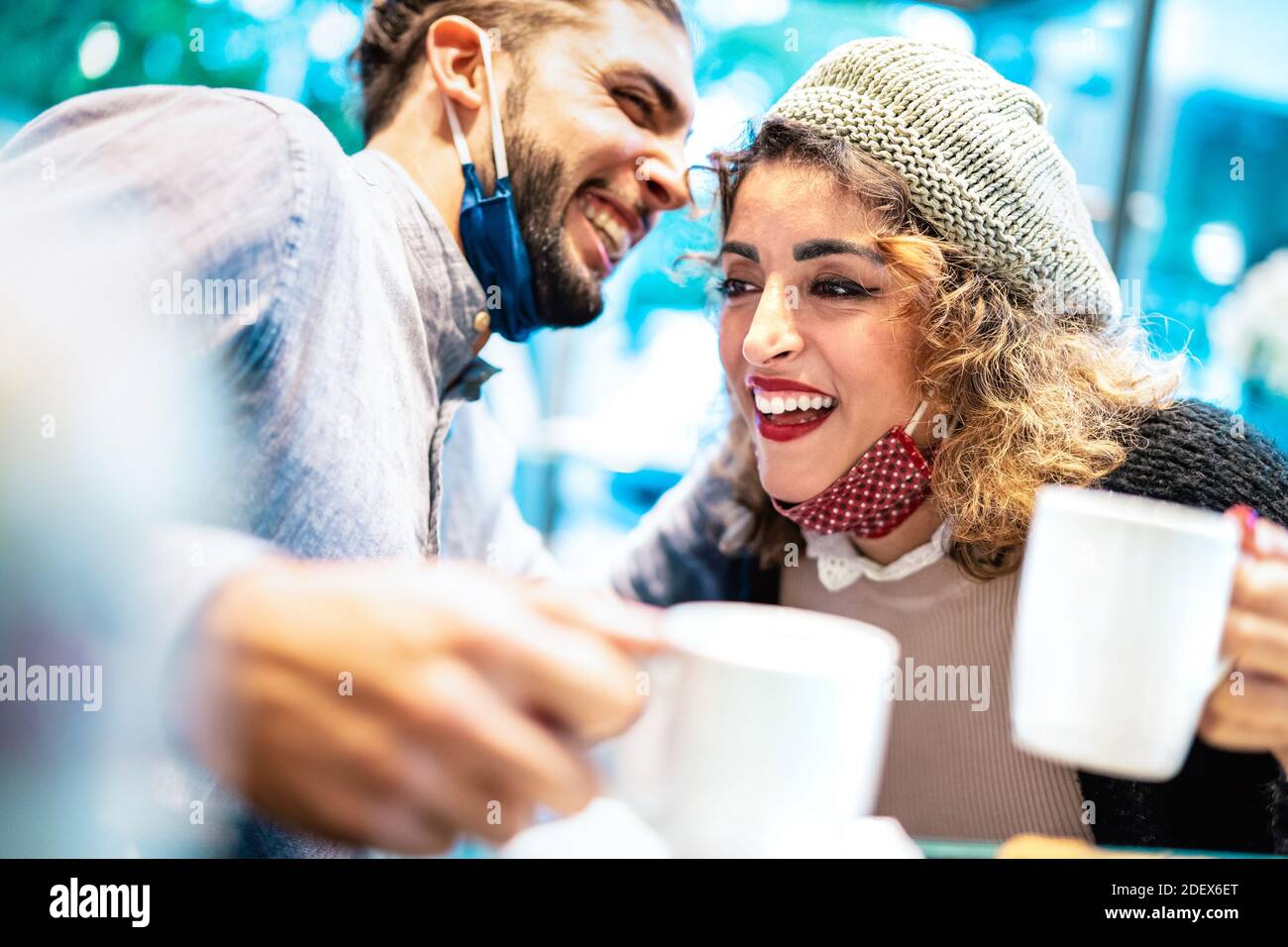 Glückliches Paar mit Gesichtsmaske Spaß zusammen an der Bar Cafeteria - Neue normale Lifestyle-Konzept mit jungen Menschen reden Und amerikanischen Kaffee trinken Stockfoto