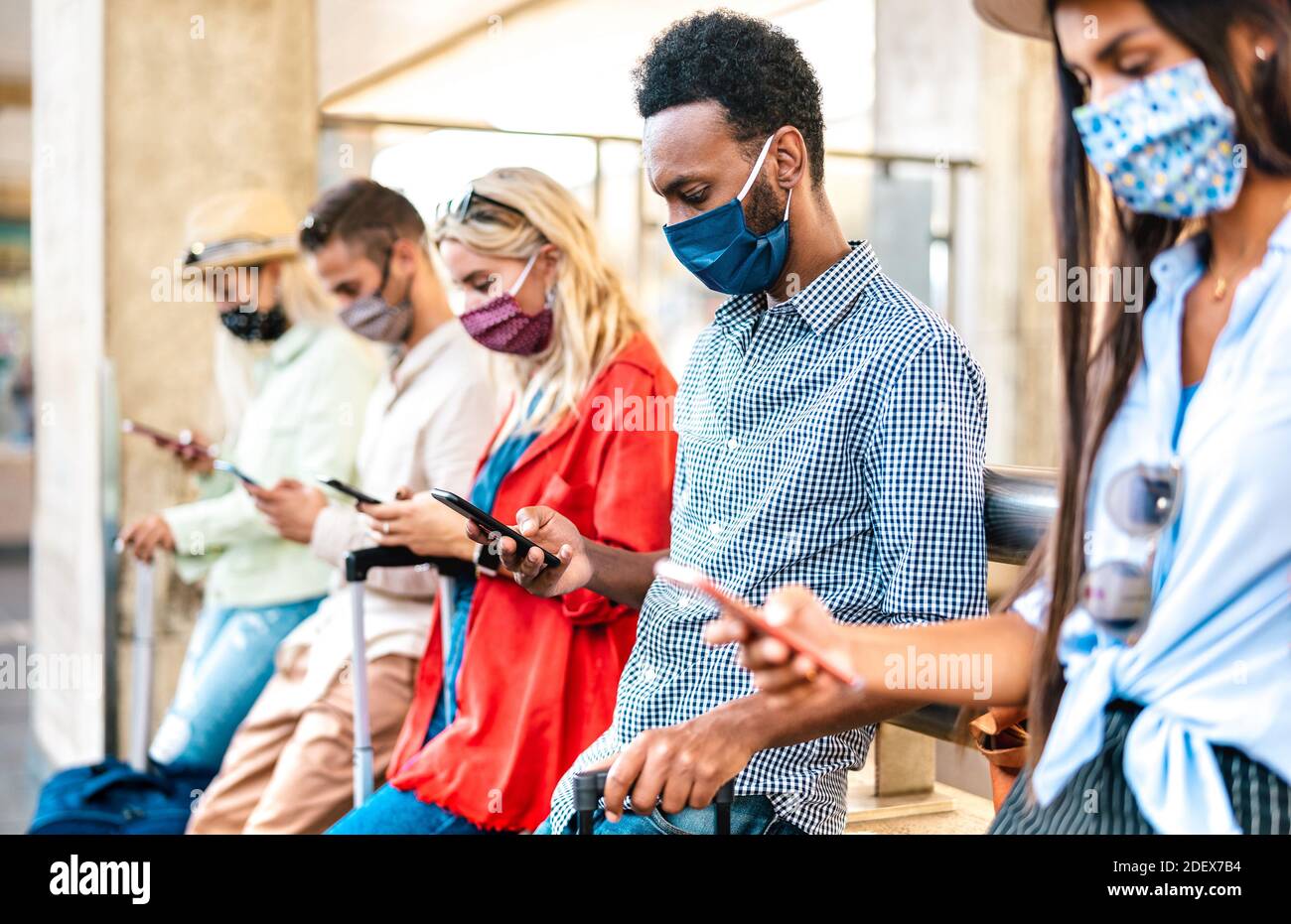 Multirassische Freunde mit Gesichtsmaske mit Tracking-App mit Handy Smartphones - Junge Menschen, die online buchen unter Bahnhof Stockfoto
